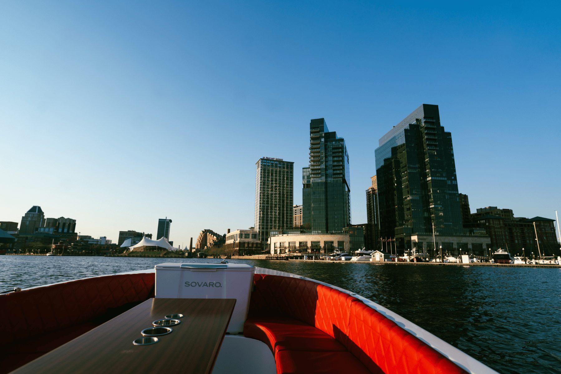 View from the red-leather deck of a Yachtsy picnic boat toward the Baltimore Inner Harbor skyline at golden hour