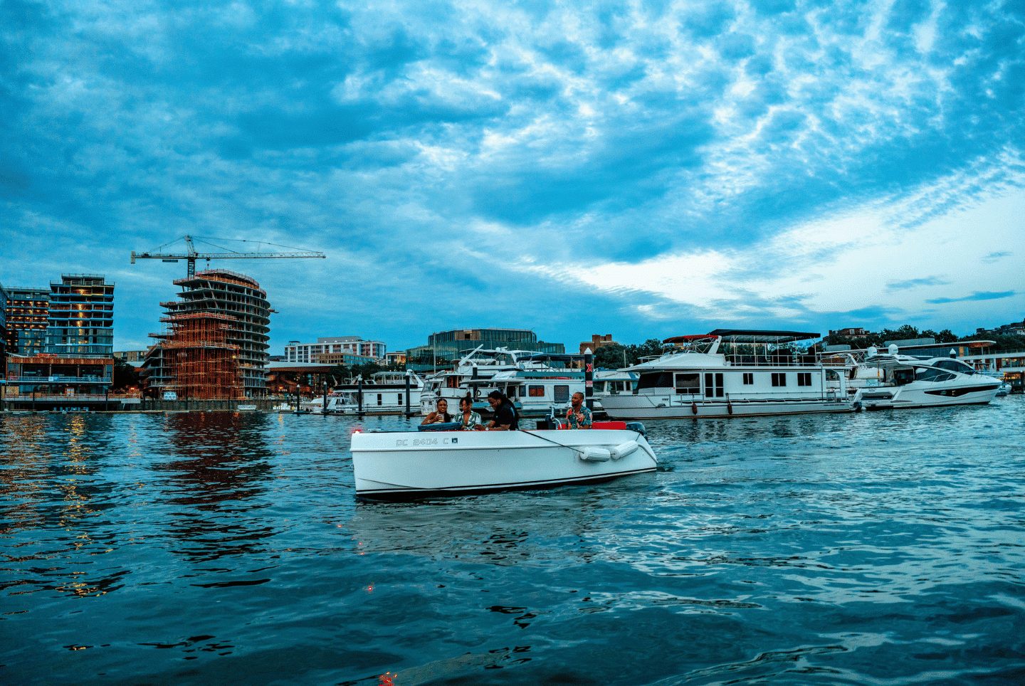 Guests aboard a white Yachtsy boat cruising the DC Navy Yard marina at dusk