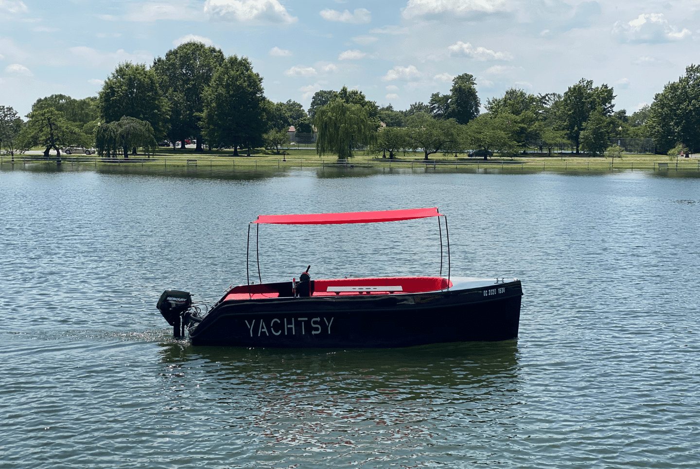 The Yachtsy picnic boat with its red canopy on calm water beside a tree-lined park