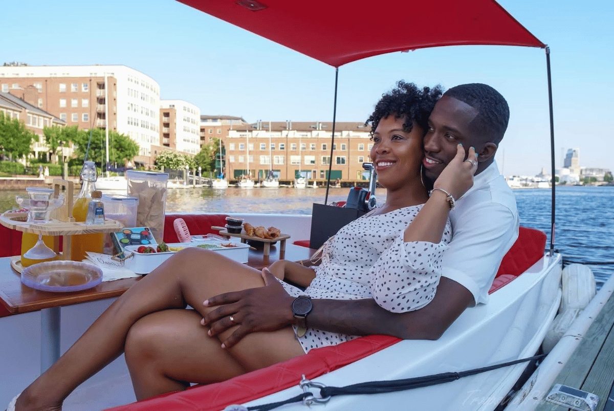 A couple relaxing under the red canopy of a Yachtsy boat with a BYO picnic spread