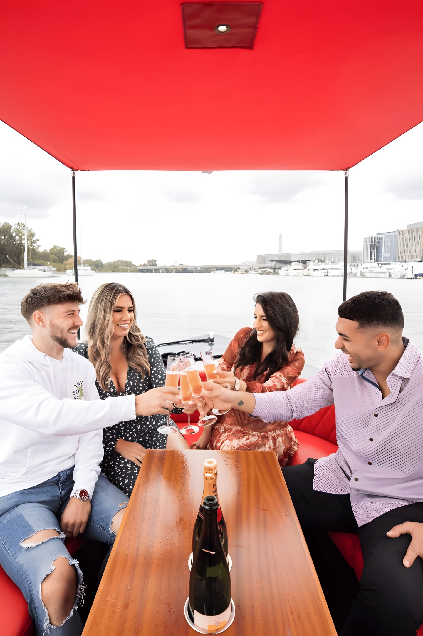 Two couples toasting champagne under the red canopy of a Yachtsy boat on the DC waterfront